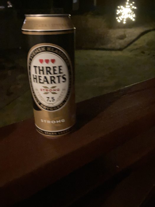 En burk öl märkt "Three Hearts Strong" på en träledge, mörk bakgrund, svag belysning, oskarp ljuskälla.