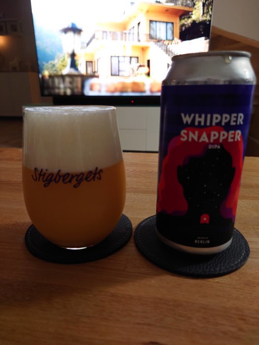 Ett ölglas med skum, en burk med etiketten "Whipper Snapper", suddig bakgrund med TV-skärm.