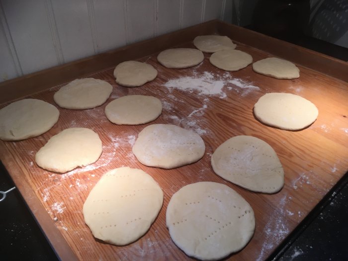 Färdigjäsad deg utplattad i olika former på mjölad träbänk, förmodligen beredning av bröd eller bakverk.