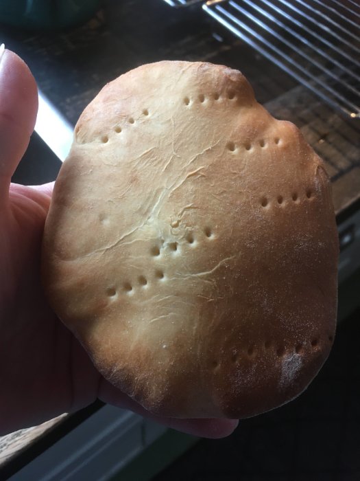 En hand håller upp ett nylagat bröd med perforeringar mot en köksbakgrund.