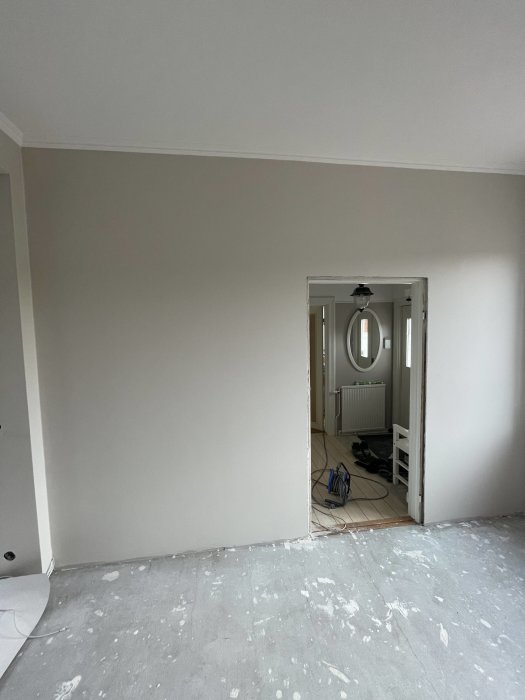 Ett rum under renovering med spackel på golvet, nakna väggar och en öppen dörr.