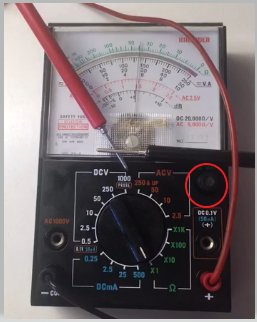 Analog multimeter med inställningar för volt, ohm, ampere. Röd och svart testkabel anslutna. Visaren indikerar nästan noll volt.