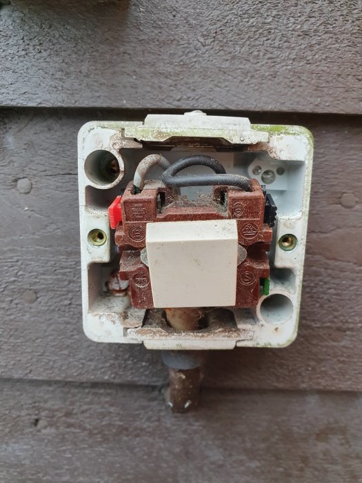 Öppen, gammal, trasig elektrisk uttagsbrytare utan frontlock, fastsatt på mörk vägg.