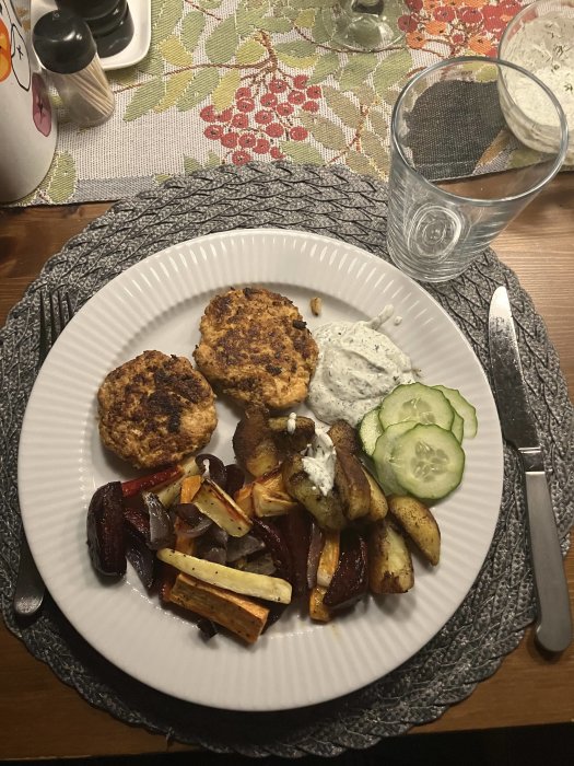 Middagsmåltid med köttbullar, rostade rotgrönsaker, tzatziki, gurkskivor, peppar och saltkar, vattenglas, blommig duk.