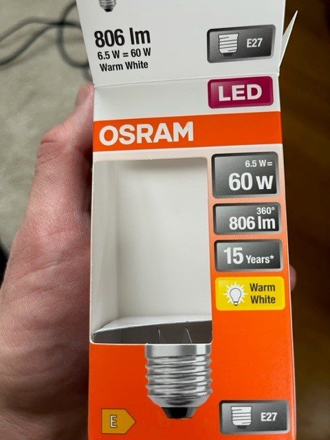 En hand håller en öppen OSRAM LED-lampförpackning som visar specifikationer men själva lampan saknas.