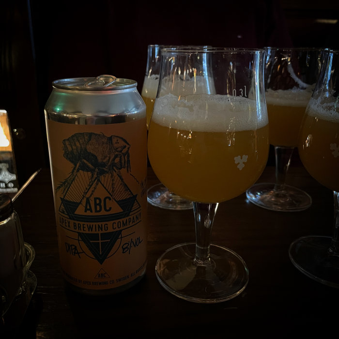 En ölburk från Apex Brewing Company bredvid tre glas fyllda med öl.
