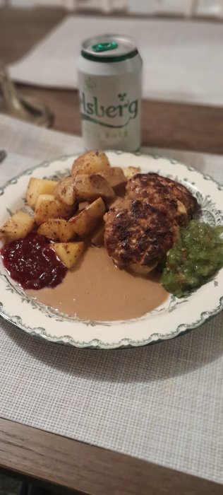 En måltid med köttbullar, klyftpotatis, lingonsylt och brunsås. Ölburk i oskärpa i bakgrunden. Hemlagad middag.