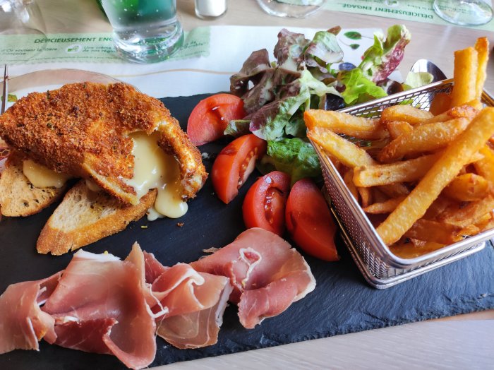 Panerad kyckling med smält ost, prosciutto, pommes frites, sallad, tomat på svart skifferplatta.