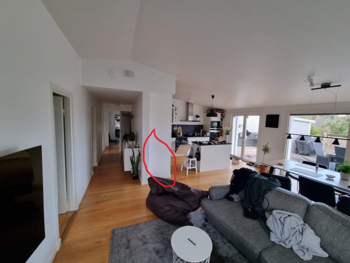 Modernt vardagsrum, kök i bakgrunden, trägolv, grå soffa, vitredskap, kuddar, ljust, rymligt, sängkläder på soffa.