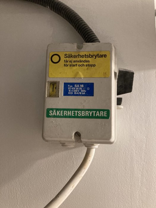 En säkerhetsbrytare med varningsetikett och ansluten kabel på en vägg.