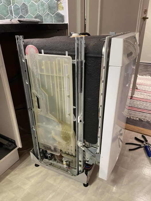 Diskmaskin liggande ner, öppnad för reparation eller service, verktyg synliga på golvet.