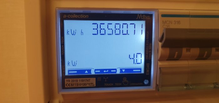 Digital energimätare som visar kilowattimmar, installerad på en vägg, med kablar och installationsdetaljer synliga.