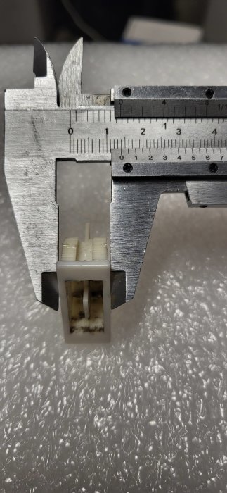 Skjutmått mäter ett litet objekt, möjligtvis en elektrisk komponent, reflekterande yta i bakgrunden.