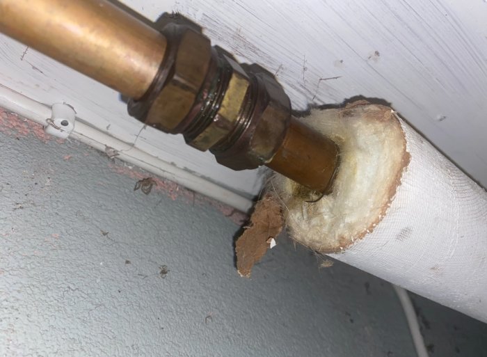 Isolerad röranslutning med värmeisolering och kopplingar, möjlig vatten- eller värmesystemdel, inomhus, närbild.