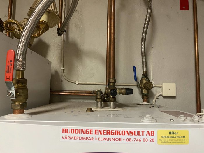 Värmepump med kopparledningar, reglerventiler, och slangar i en teknisk installation. Etiketter och företagsnamn synliga.