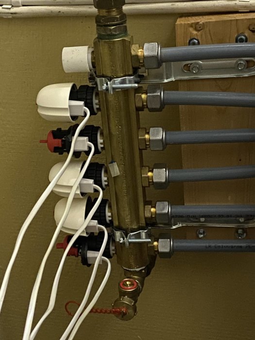 Golvvärmefördelare med termostatventiler och flödesmätare, rör och elektriska kablar synliga.