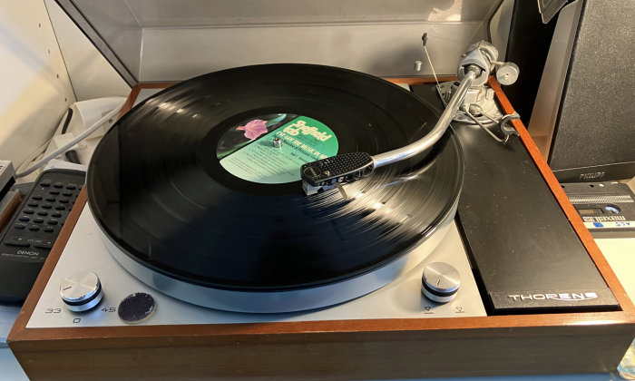 Vinylspelare med skiva, Thorens-varumärke, tonarm, hastighetsreglering, spelar musik, interiör, elektronik, nostalgisk.