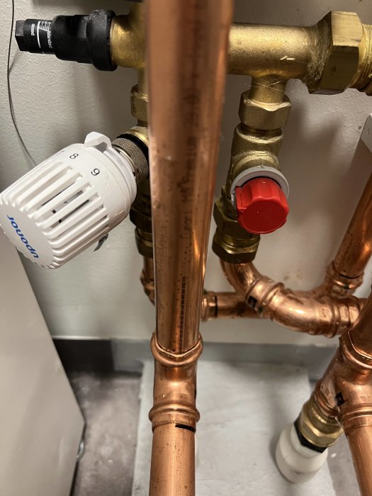 Kopparledningar, termostatventil, avstängningsventil, VVS-installation, vita och röda justeringsrattar.