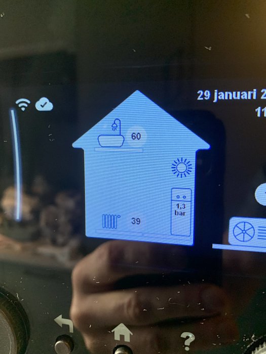 Digital husformad display visar temperatur, vattenförbrukning och tryck; datumtid uppe till höger; spegling av hand undertill.