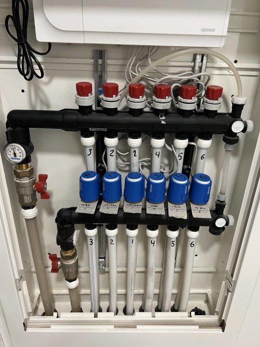 Installationscentral för golvvärme med flera reglerventiler, rör och manometer. Märkt och ordnat i ett skåp.