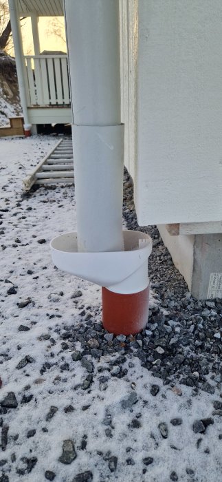 Avloppsrör med förlängningsdel och bred fångbricka på grus med lite snö. Veranda i bakgrunden.