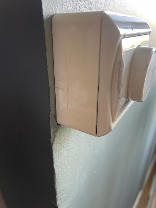 Vit termostat på vägg, närbild, ojämn väggkant, skuggor, inomhus, dagljus.