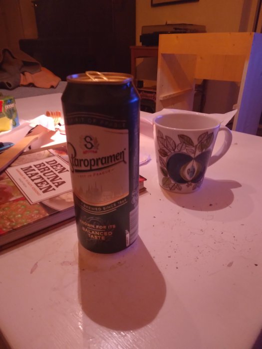 Ölburk och kaffekopp på bord med skuggor, oordning i bakgrunden.