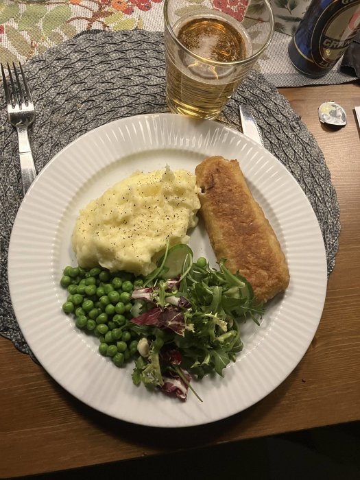 En måltid med mosad potatis, panerad fiskfilé, gröna ärtor, sallad och ett glas öl.