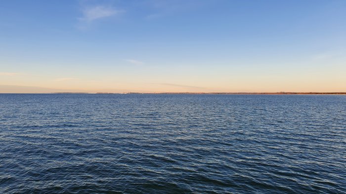 Vattenyta med vågor, horisont vid klar himmel, lugnt, kvällsljus, möjlig kustlinje i fjärran.