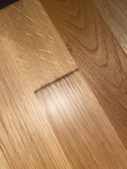 Trägolv med en uppåtvikt hörna på en tunn träplatta eller folie. Skuggor och ljusspel. Warma bruna toner.