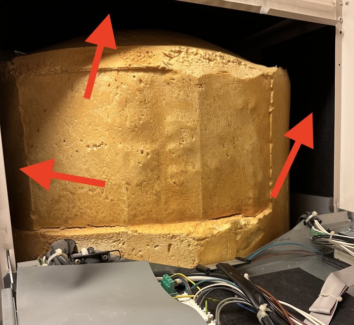 En gul skumisolering med röda pilar, dolt elektronikskåp, otydligt objekt i förgrunden.