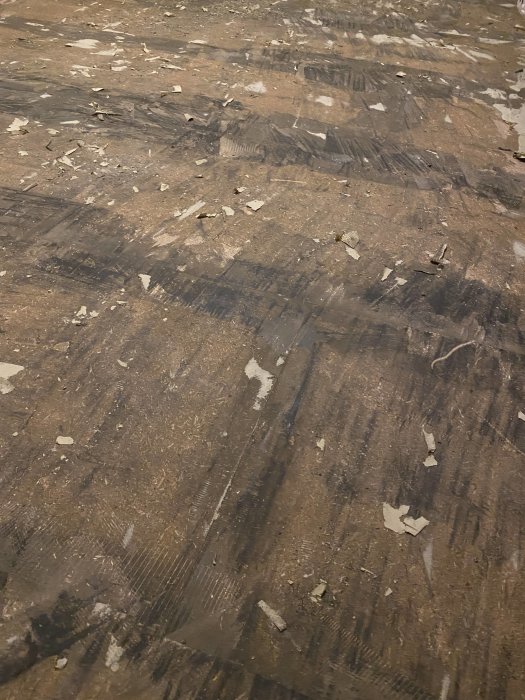 Slitet trägolv med rester av vit färg och märken. Nedskräpat, behöver underhåll eller renovering.