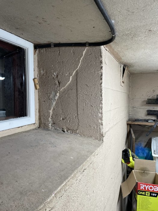 Ett slitna garagehörn med spruckna betongväggar, ett fönster och verktyg.