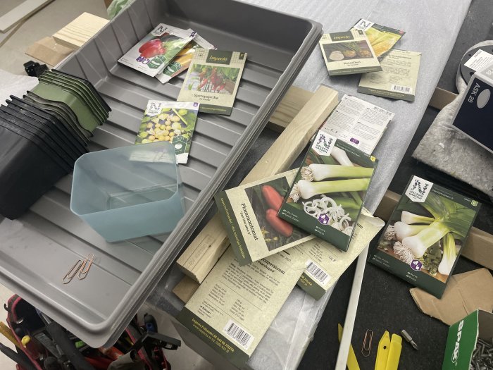 Oorganiserad arbetsyta med plantpaket, krukor, verktyg och skräp; trädgårdsförberedelse, oordning.