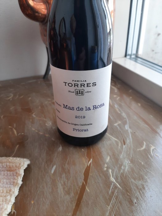 Vinflaska på bord nära fönster, etikett säger "Familia Torres", "Mas de la Rosa" 2019, Priorat.
