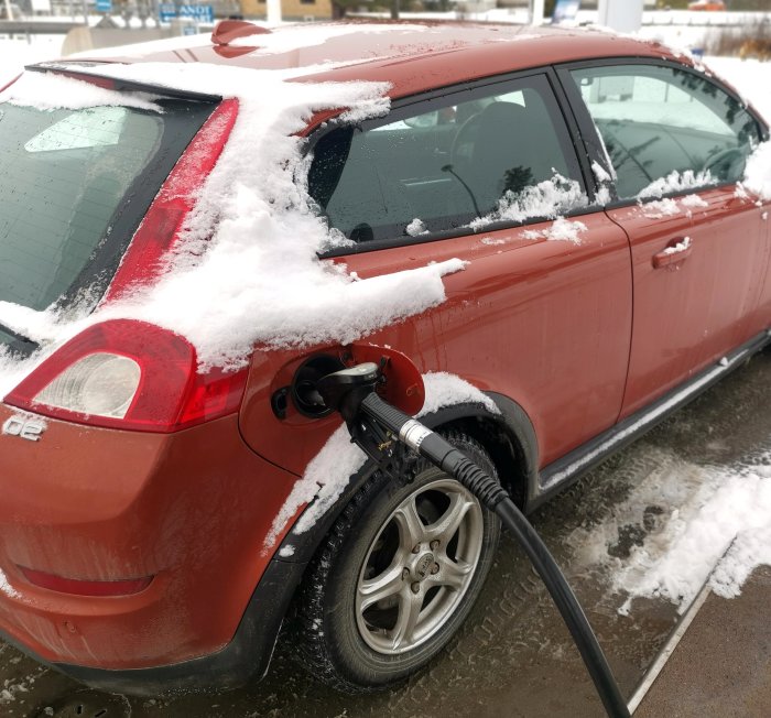 En röd bil täckt med snö tankas vid en bensinstation på vintern.
