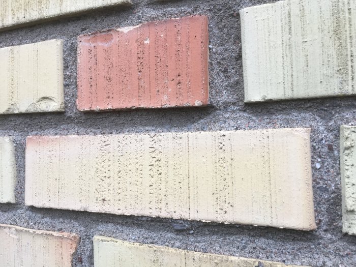 Vägg av variabeltfärgade tegelstenar med mörtel i ljusdagsljus, textur, mönster.