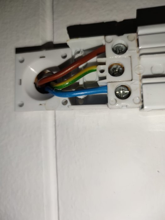 Eluttag under installation, färgkodade kablar synliga, mot en vägg, säkerhetsrisk om strömmen är påslagen.