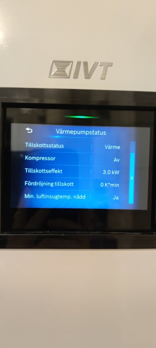 Digital kontrollpanel för värmepump som visar statusinformation och driftdata på svenska, inramat av vit apparat.