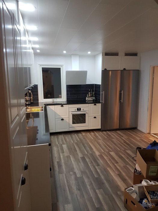 Modernt kök med vit inredning, rostfritt kylskåp och träfärgat golv. Inbjudande och ljust.