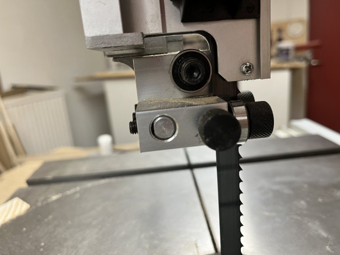 Bandsåg närbild, metallkonstruktion, sågblad, justeringsrattar, träbearbetningsverktyg, arbetsbänk bakgrund.