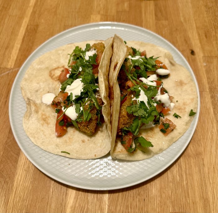 Två fyllda tacos med sås, koriander och tomat på en tallrik.