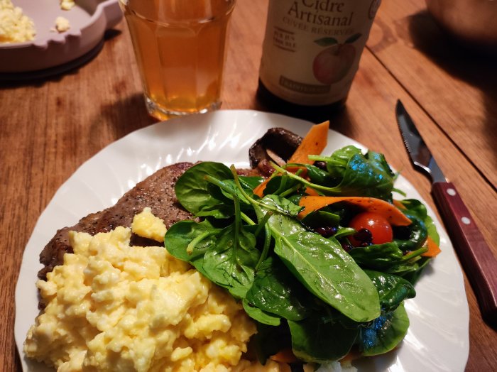 Middagstallrik med kött, mosad potatis, sallad, glas med dryck och äppelciderflaska i bakgrunden.