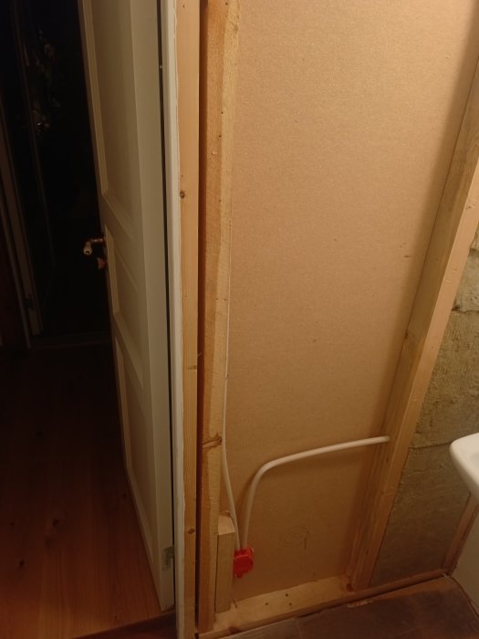 Oavslutad inomhusrenovering, träreglar, spånskiva, synliga rör, dörröppning, ogjort elarbete, otydlig teckning på väggen.