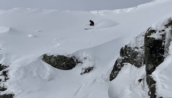 Skidåkare utför snötäckt bergssluttning bland klippor, dimmigt, vinteraktivitet, utomhusäventyr, friåkning.