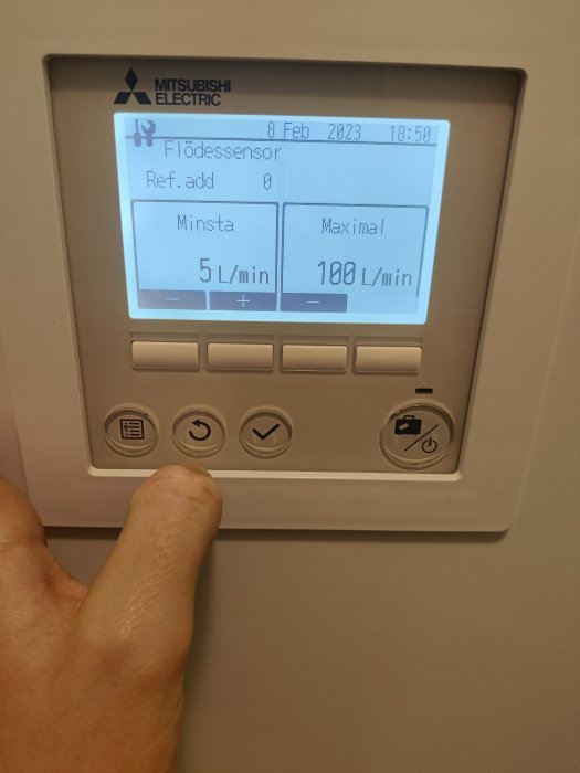 En hand använder Mitsubishi Electric enhetens gränssnitt, visar flödessensorinställningar, datum och tid.