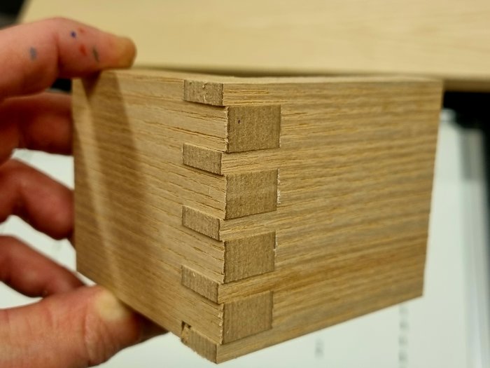 En hand håller i en stapel av rektangulära träbitar, möjligtvis material för modellbygge eller hantverk.
