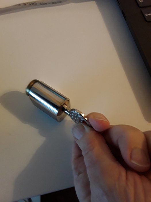 En hand håller en metallisk ljudpinne nära ett vitt papper på ett skrivbord.