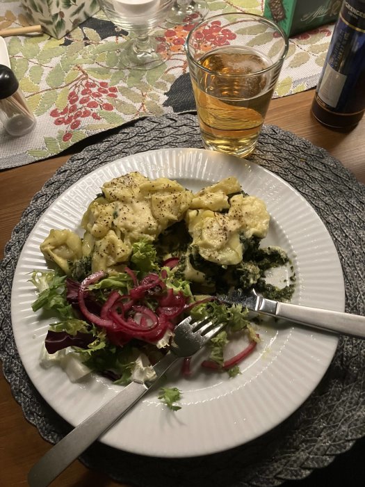 Ett måltid med pasta, sallad och picklad rödlök, serverat med ett glas dryck.