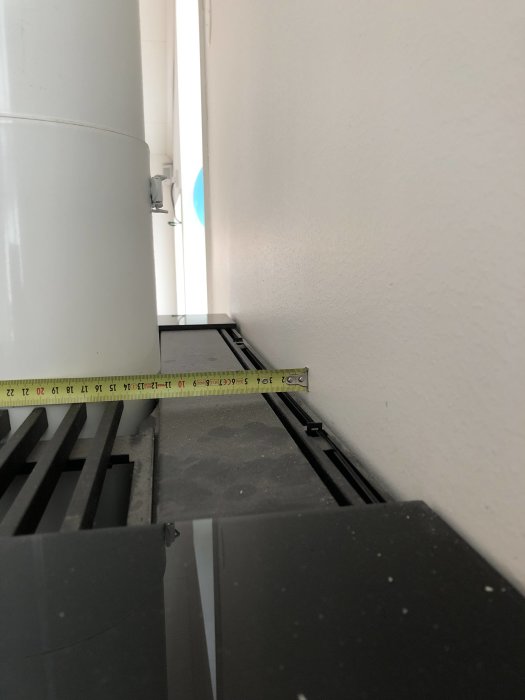 Måttband mäter avstånd mellan vit vägg och svart yta inomhus.